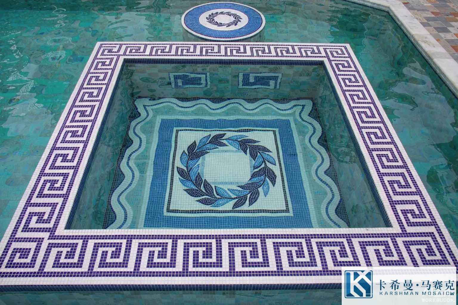 Aerial view of a Mediterranean swimming pool floor decorated with a glass mosaic Greek key border and a laurel wreath medallion in blue and white