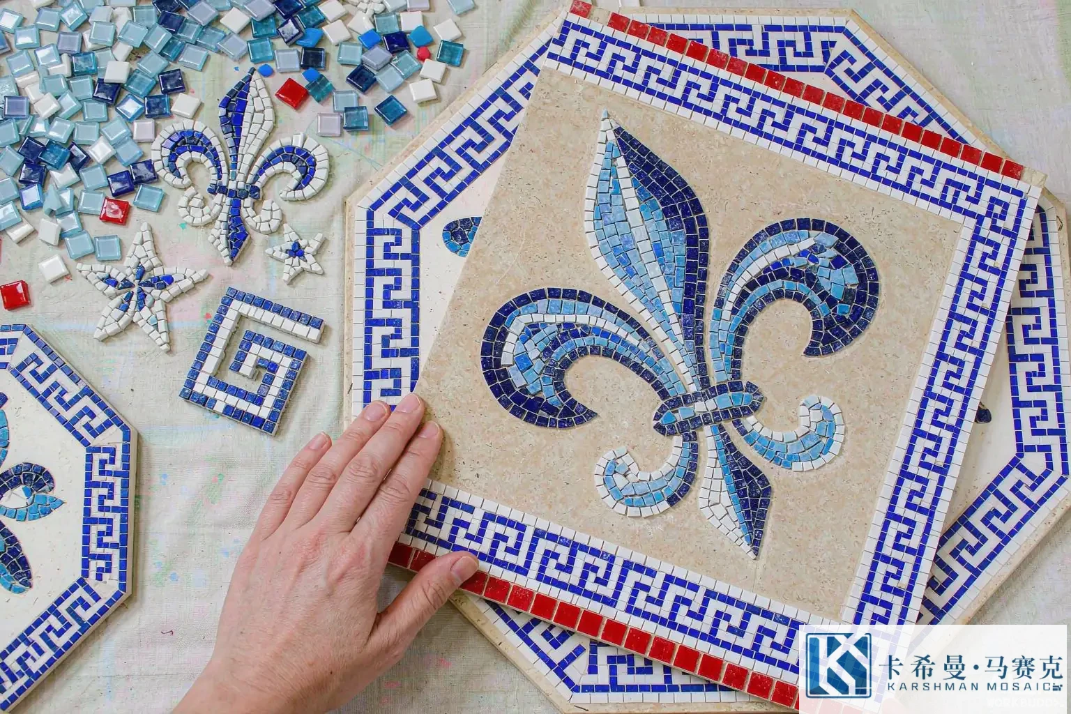 Top view of a hand laid European mosaic panel with loose glass tiles shaped like a fleur de lis and Greek key