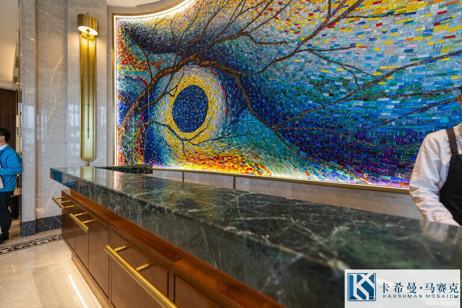 Elegant hotel lobby reception with a large glass mosaic mural on the wall behind the desk, warm ambient light