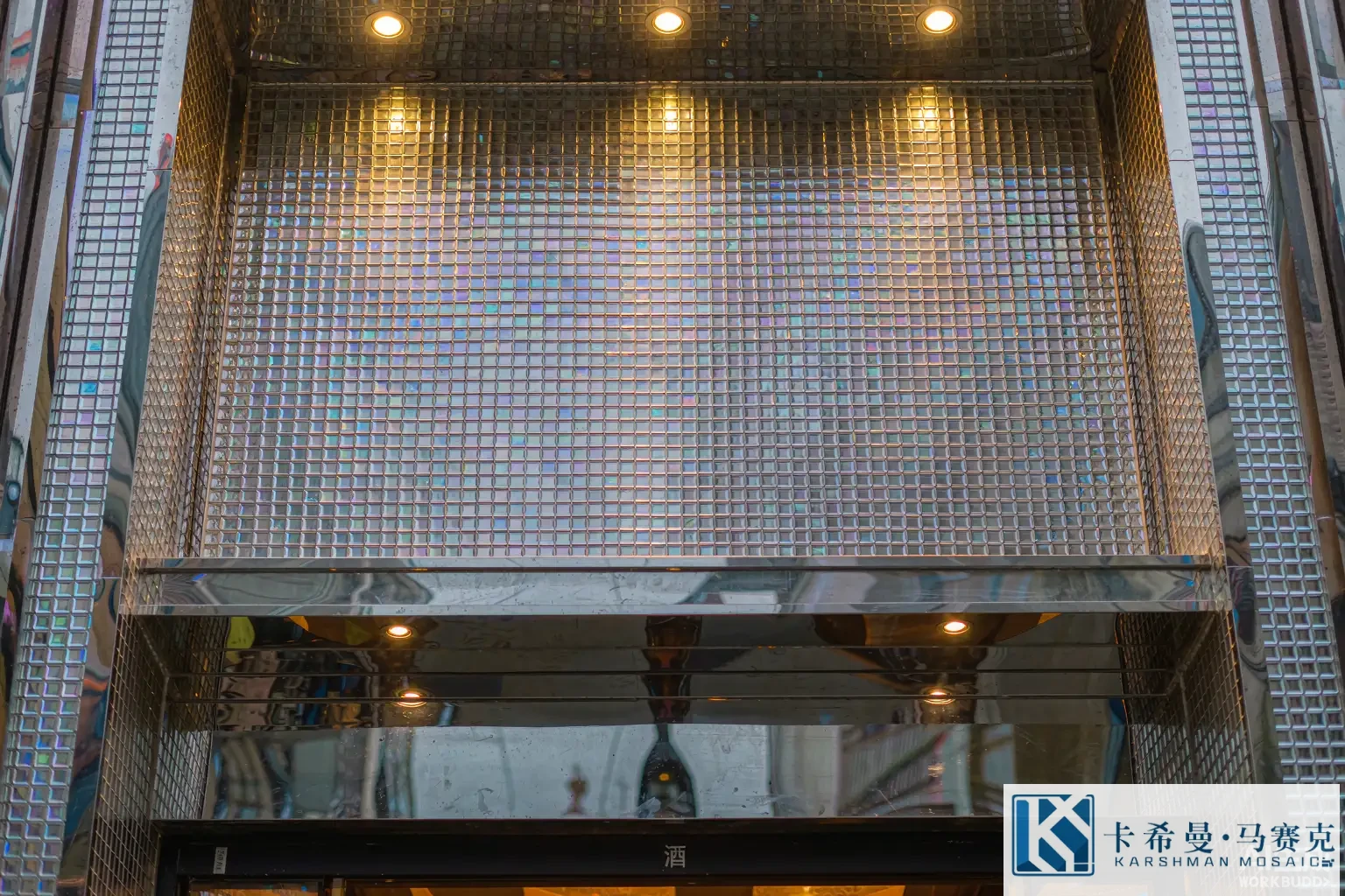 Restaurant bar front clad in iridescent glass mosaic tiles under warm spotlights, reflective detail